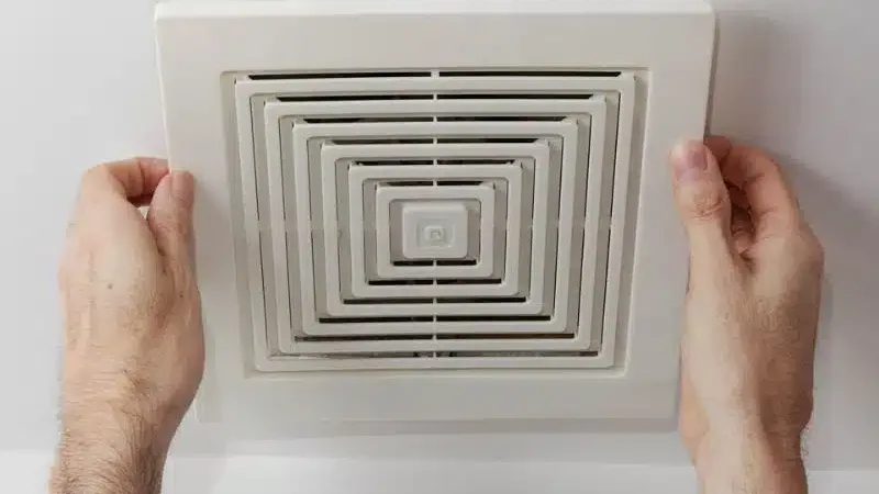 Bathroom exhaust fan grille held up to the ceiling